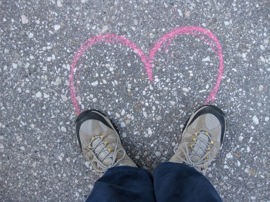 Photo of a heart outlined on the pavement in chalk, completed by feet at the bottom of the heart